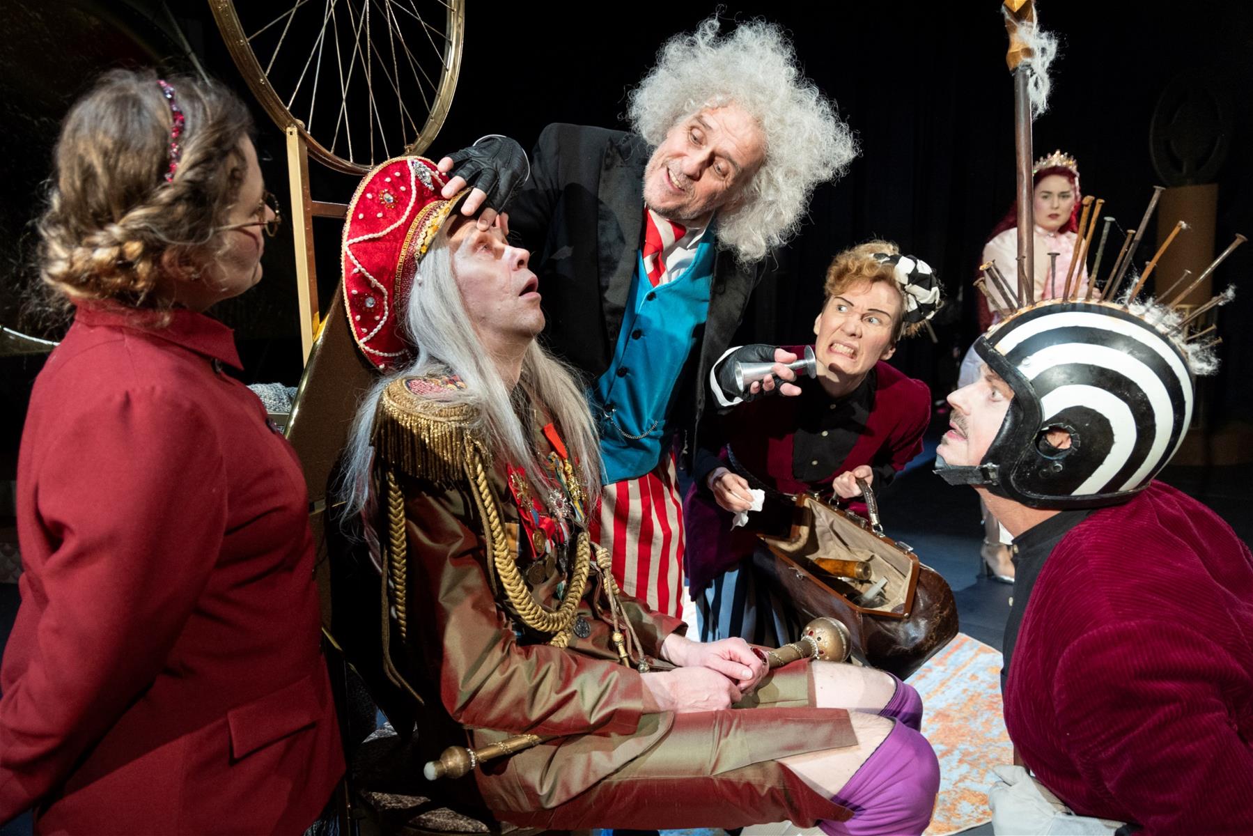 Kohtaus näytelmästä. Diktaattoriasuinen mies istuu valtaistuimella tuskaisen näköisenä. Hänen ympärillään seisoo viisi ihmistä, jotka kaikki katsovat miestä.