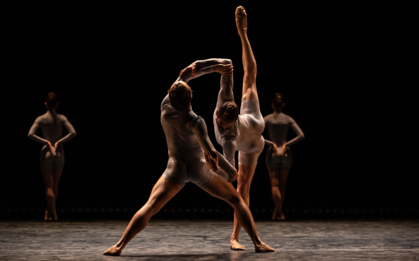 Etualalla kaksi balettitanssijaa tanssimassa dramaattisessa, hämärässä valaistuksessa. Taustalla näkyy kahden muun tanssijan hahmot.